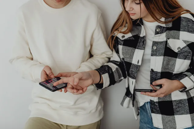 Teenagers interacting with smartphones, sharing content, and discussing technology indoors. Teen Social Media Safety: How to Check What the Algorithm Sends Your Kid